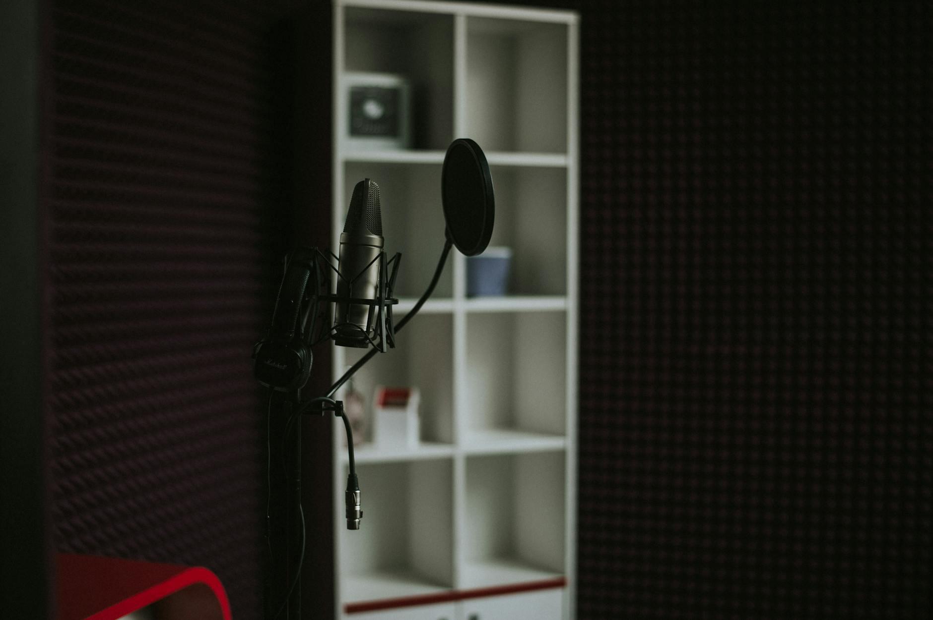 Close-up of a condenser microphone in a soundproof recording studio with modern shelving.